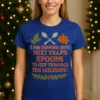 Shown on Straight Fit (S–L) body wearing royal blue T-shirt with 'I am dipping into next year's spoons to get through the holidays' unseen illness awareness design, standing in a cozy Christmas living room with holiday lights and wreath